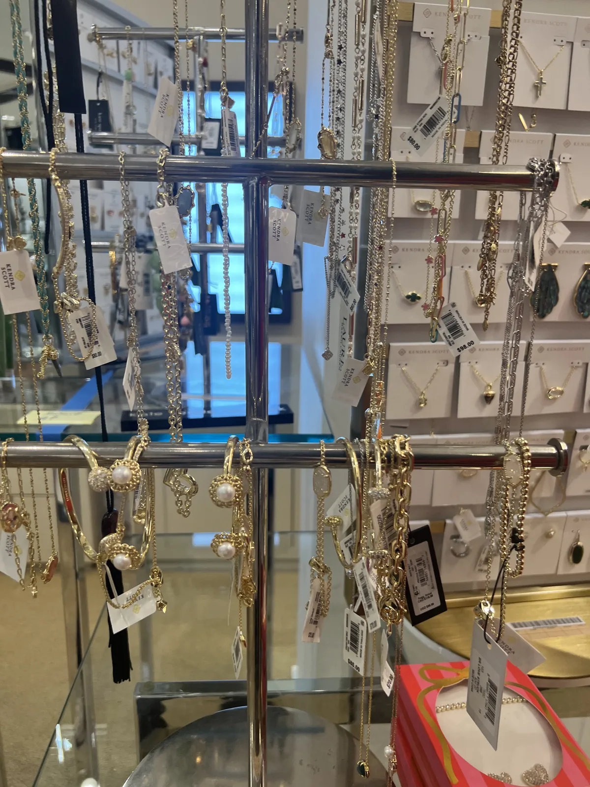 Bloomingdale's 内 Kendra Scott 旋转链塔,挂满金色链条与吊坠,墙上是品牌卡片
