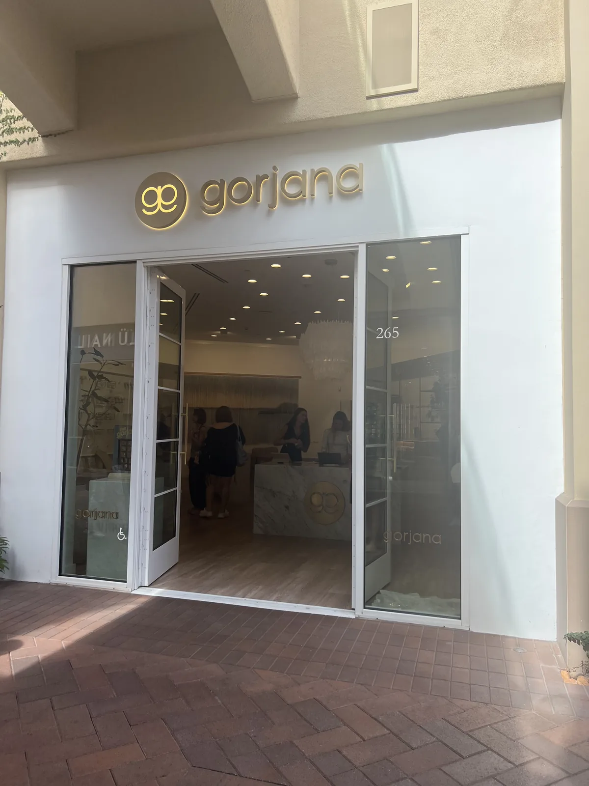 gorjana 敞开的玻璃门,店内大理石收银台带金色 gg logo,店员与顾客