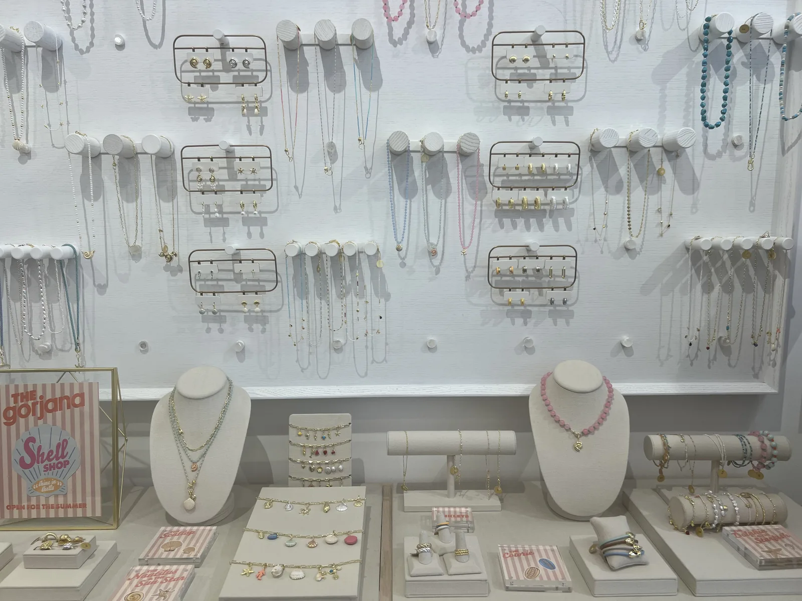 gorjana Shell Shop 陈列墙,白色挂钉板上的耳饰项链,busts 上叠戴细链,粉白条纹 Shell Shop 招牌