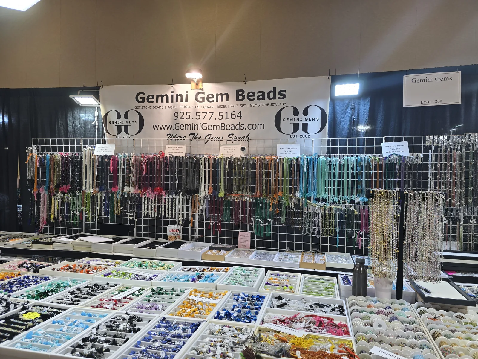 InterGem 展会 Gemini Gem Beads 散珠摊位,墙上垂挂彩色宝石珠链,桌上分格摆裸珠