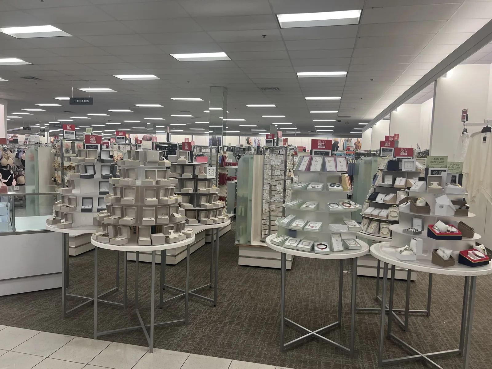 Kohl's 珠宝配饰区全景,多座圆形礼盒陈列塔与玻璃柜,紧邻内衣区 INTIMATES
